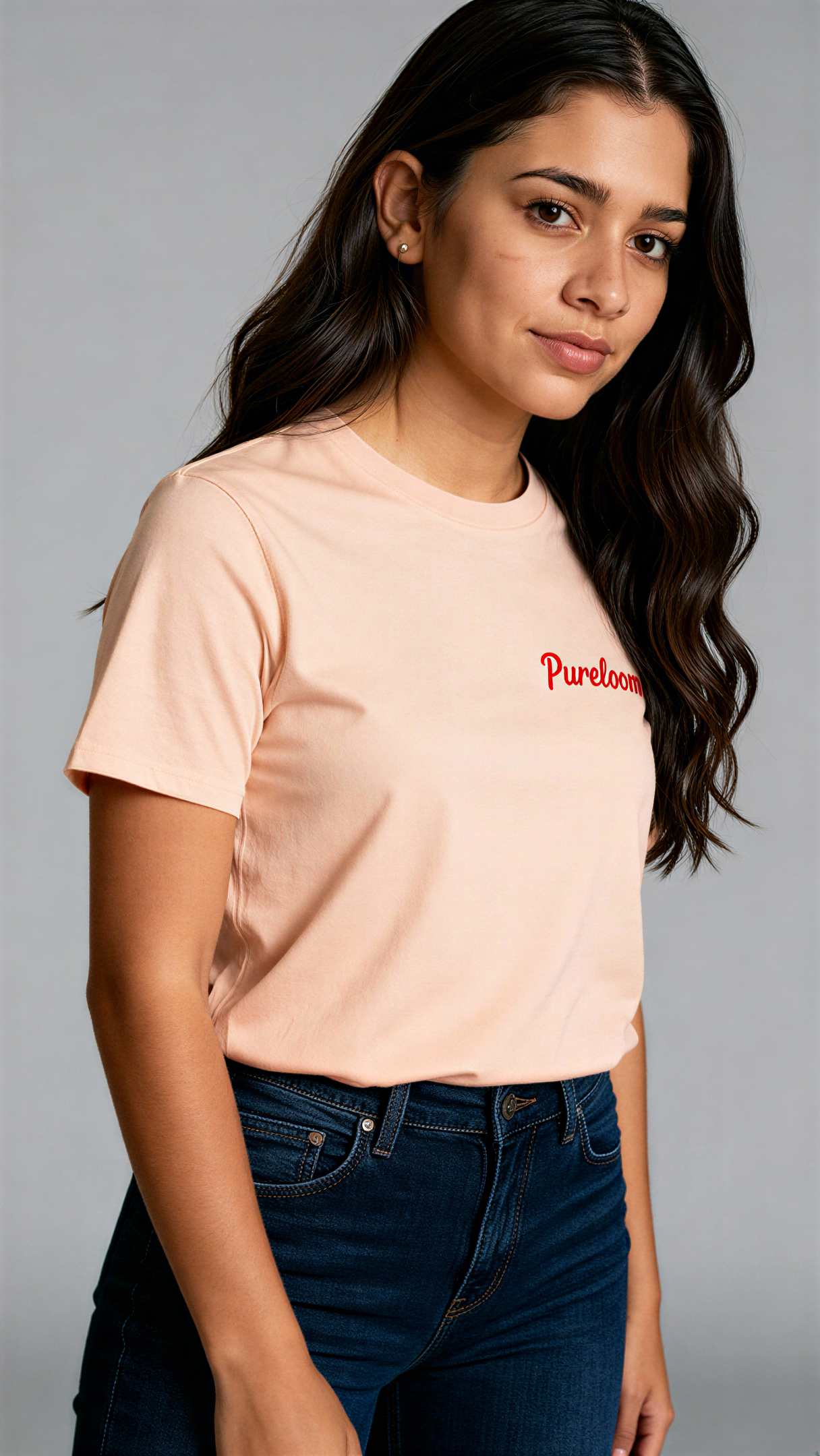 במבט צדדי, אישה לובשת חולצת כותנה אורגנית בצבע ורוד עם לוגו אדום "Pureloom" בצד שמאל של החזה מבית פיורלום.